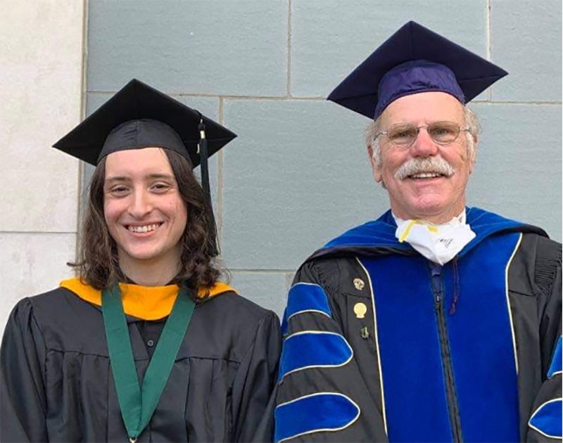 Graduate in a cap and gown standing next to a professor in academic regalia, both smiling.